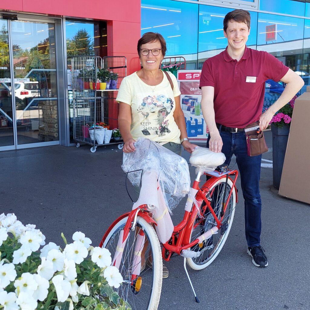 Gewinnerin und Mitarbeiter mit Fahrrad vor dem Markt